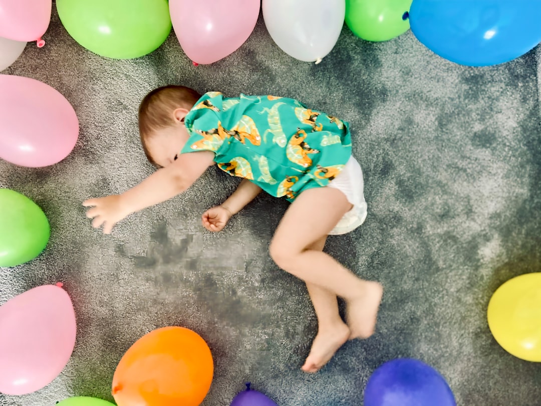 Baby boy surrounded by colorful balloons on the floor.