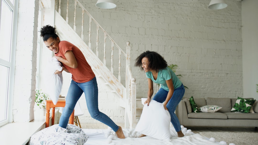 Two women having a pillow fight on a bed.