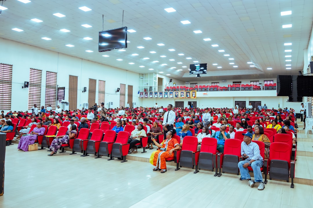 Large auditorium filled with people sitting in red chairs.